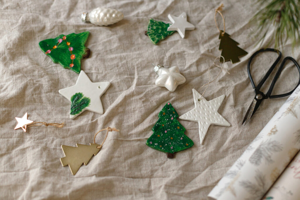 Handmade air-dry clay Christmas ornaments shaped like stars and trees, painted green and white on linen fabric.