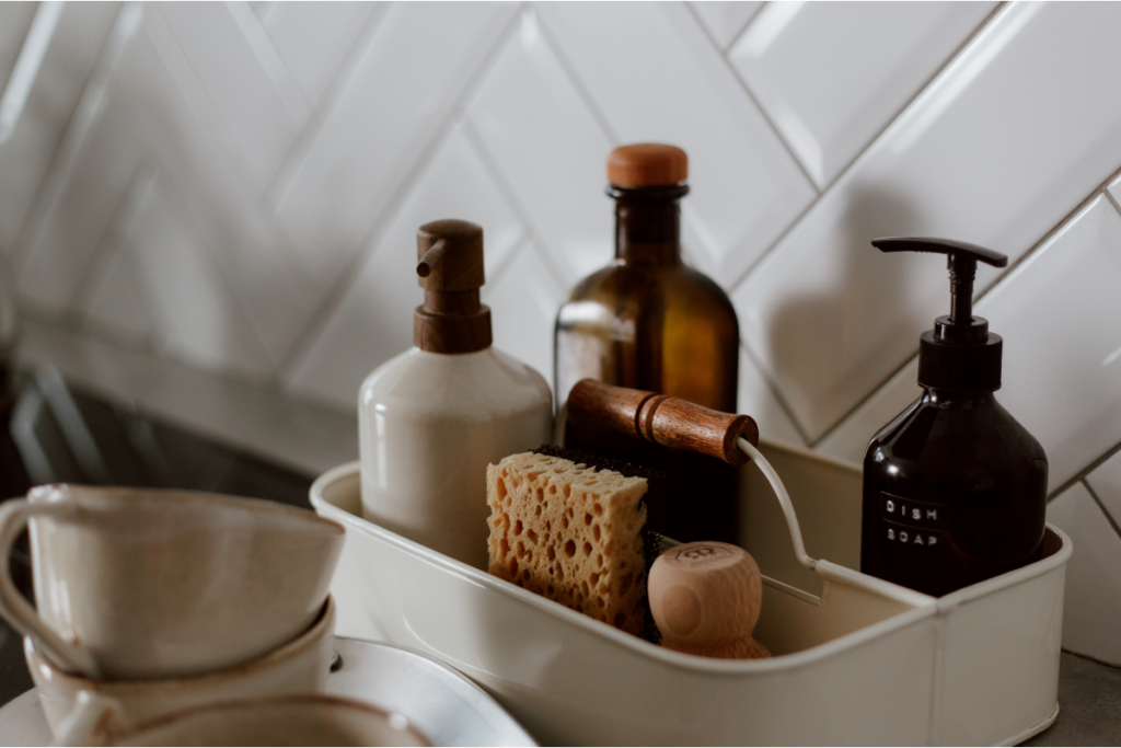 Cleaning supplies organized in a white caddy beside the kitchen sink, including soap bottles, sponges and a wooden brush.